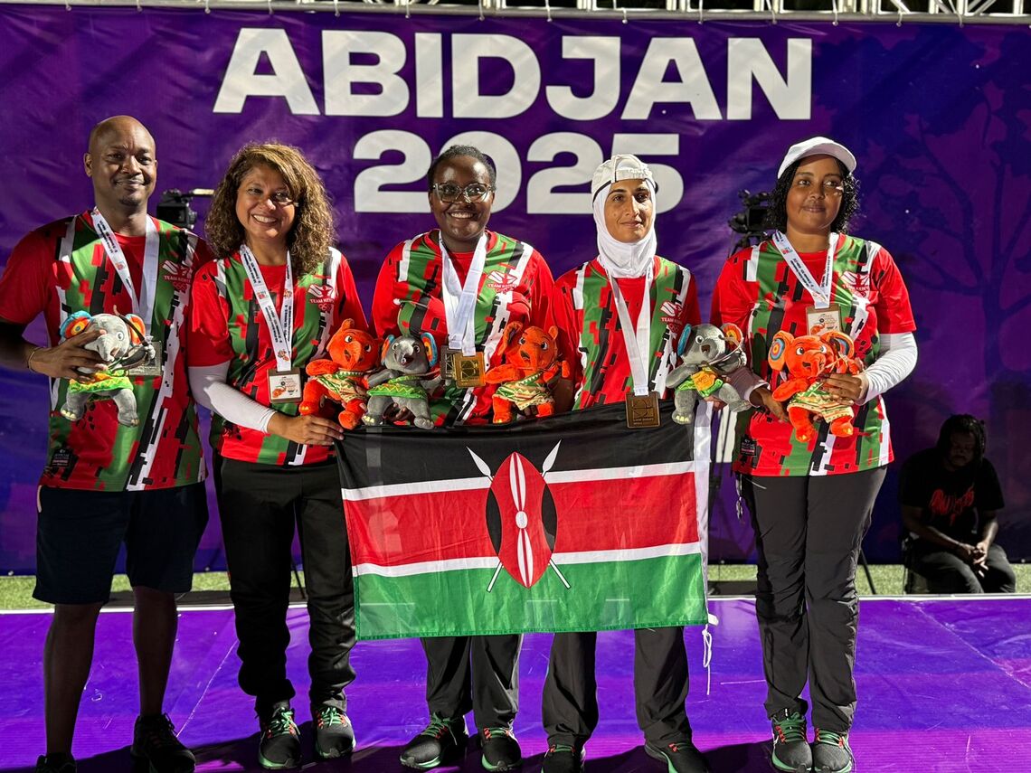 Gloria Kitali holding the Kenya flag with her fellow Kenyan archers at Abidjan 2025.
