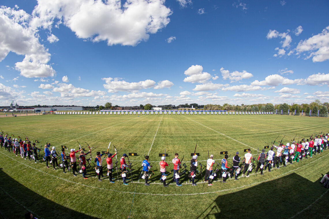 A row of archers standing on the shooting line preparing to shoot arrows at targets.