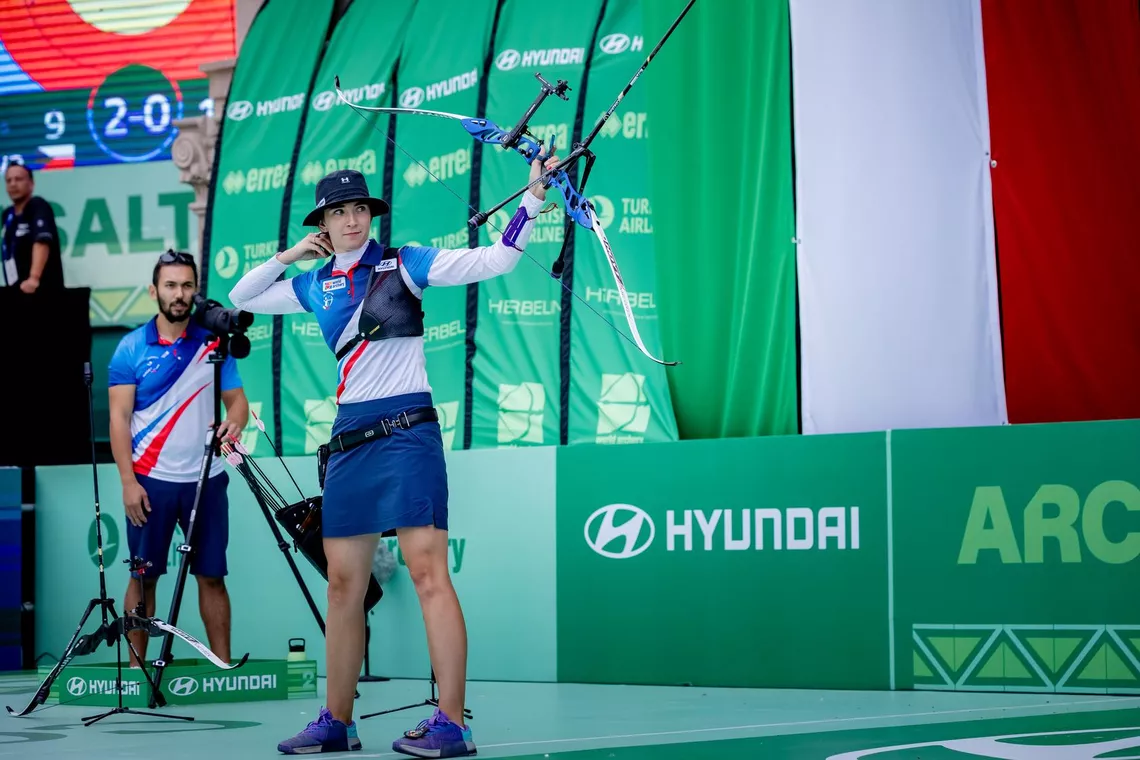 Marie Horackova watches her arrow just after release with coach and boyfriend Adam Li behind her in coaching box at Saltillo 2026.