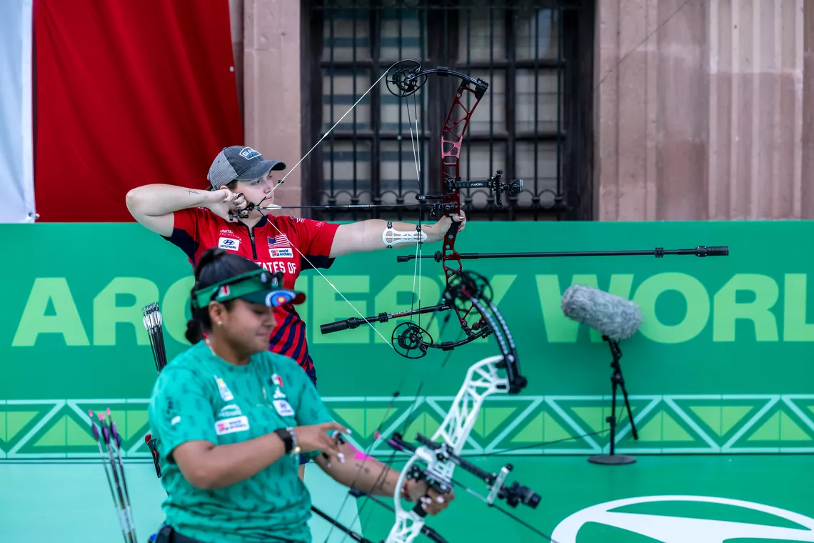 Alexis Ruiz aiming with Dafne Quintero in the background. 