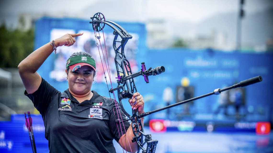 Andrea Becerra pointing to her bow after winning gold.